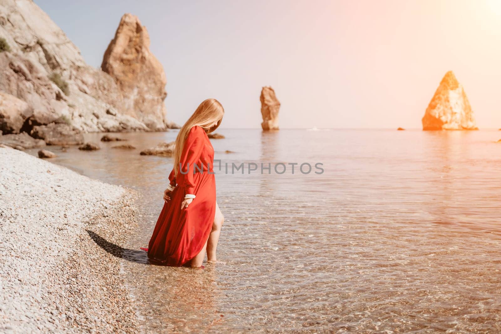 Woman travel sea. Happy tourist in red dress enjoy taking picture outdoors for memories. Woman traveler posing on the rock at sea bay surrounded by volcanic mountains, sharing travel adventure journey by panophotograph