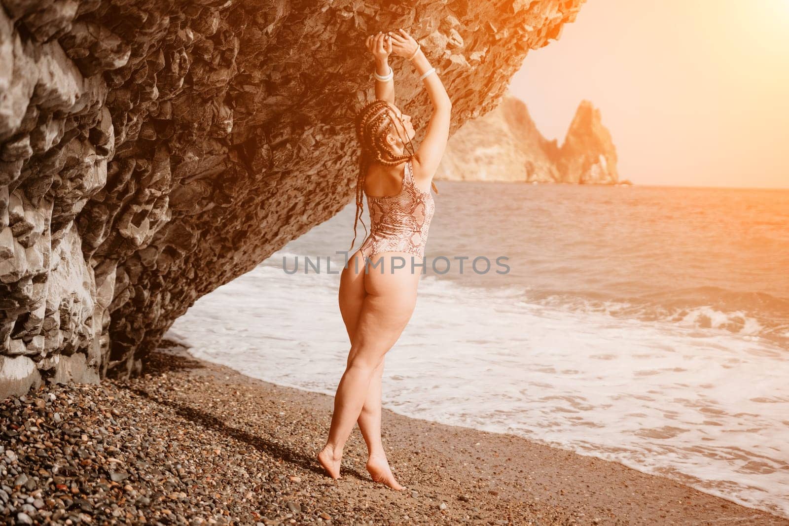 Beach vacation. Hot beautiful woman in sunhat and bikini standing with her arms raised to her head enjoying looking view of beach ocean on hot summer day.