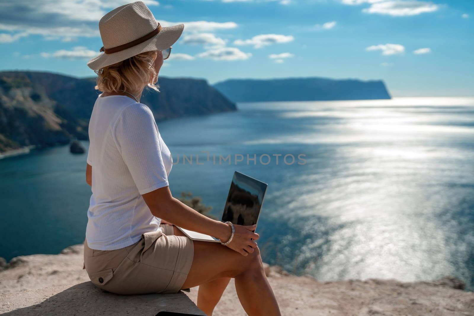 Freelance women sea working on the computer. Good looking middle aged woman typing on a laptop keyboard outdoors with a beautiful sea view. The concept of remote work