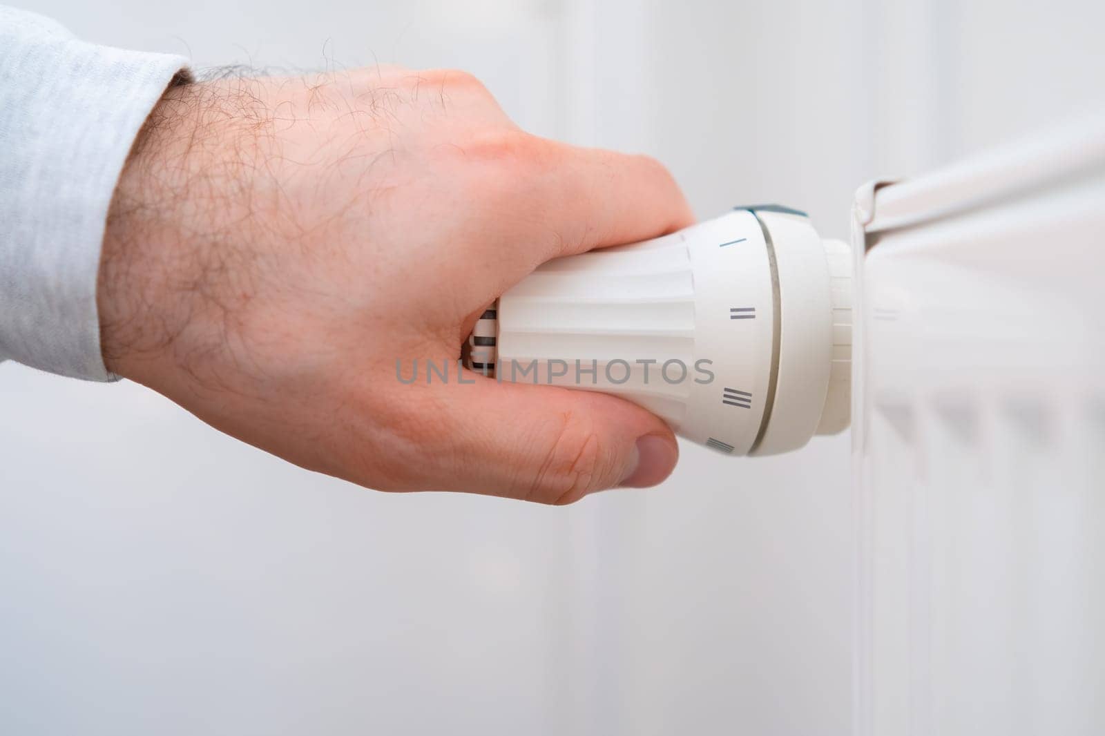 Man hand regulates temperature knob of the heating radiator to reduce heating costs.