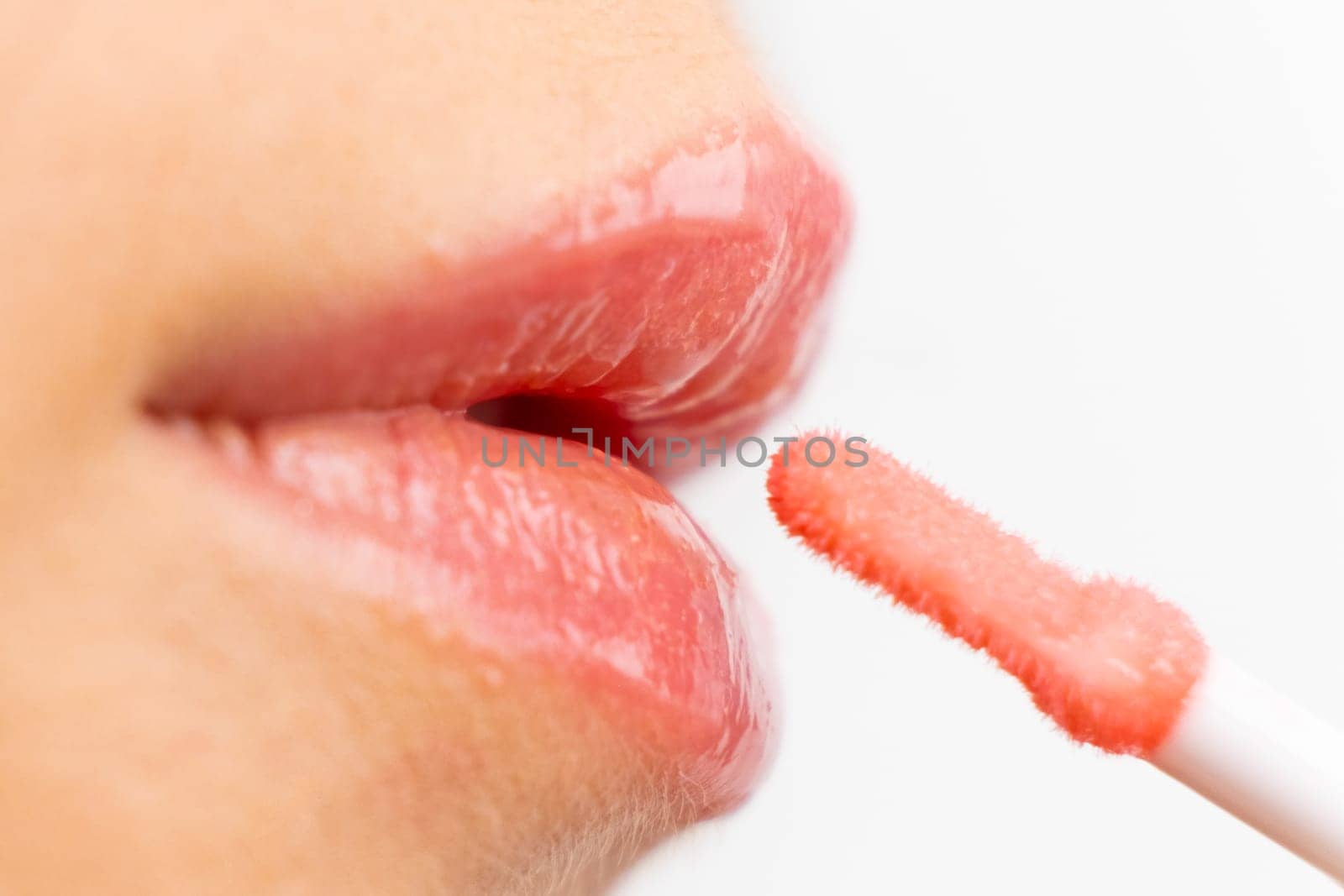Close up woman applying pink moisturizing lip gloss on the white background by vladimka