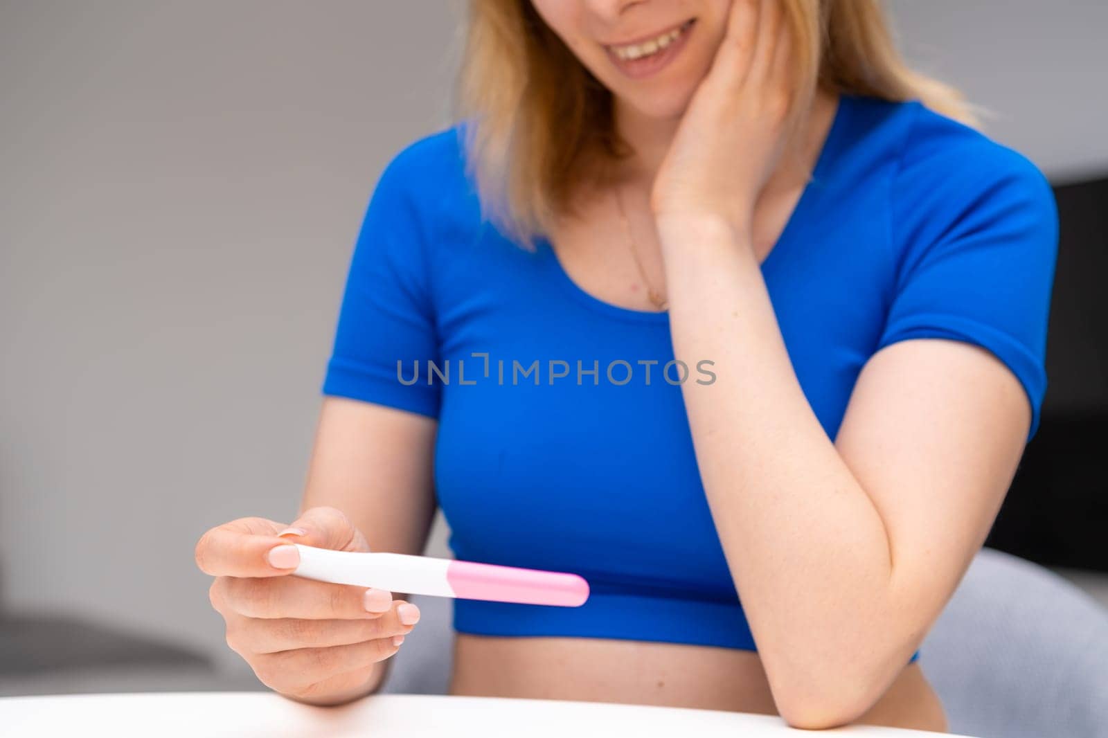 Smiling woman sitting at the table and holding the pregnancy test. Expectation of baby.