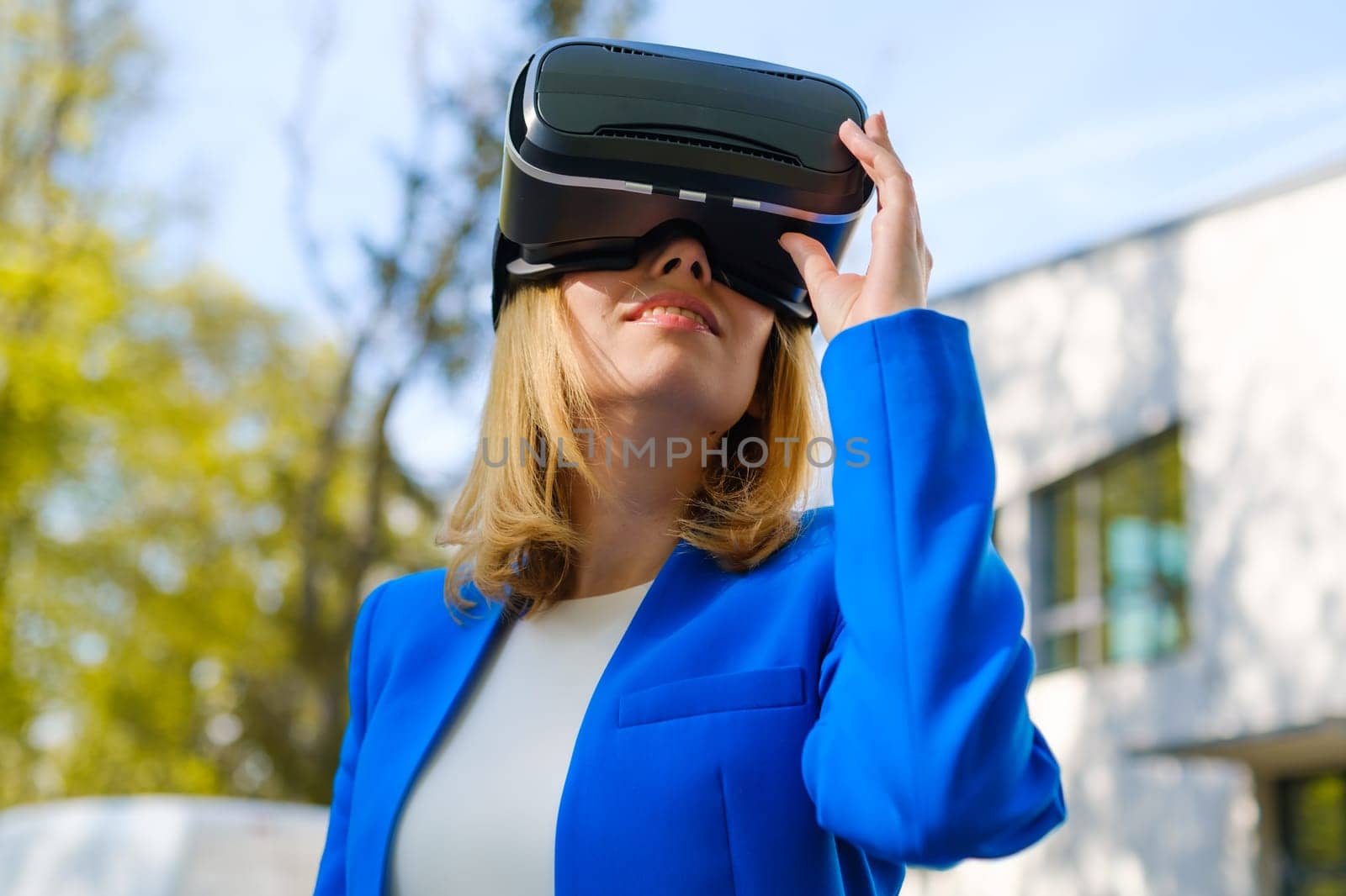 Smiling woman in vr glasses experiencing augmented reality in front of a business center. Futuristic future in the metaverse world.