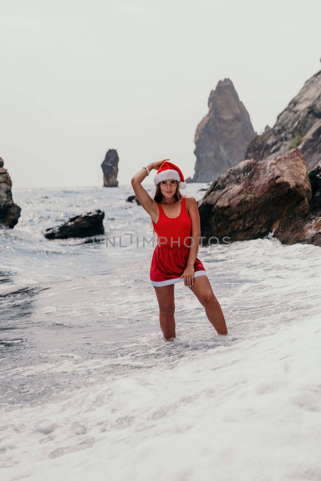 Woman travel sea. Young Happy woman in a long red dress posing on a beach near the sea on background of volcanic rocks, like in Iceland, sharing travel adventure journey