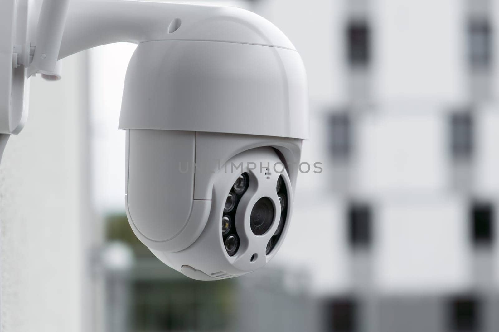 Modern CCTV camera on a wall with a blurred multi-storey building on the background. Surveillance and monitoring of outdoor to protect against thieves