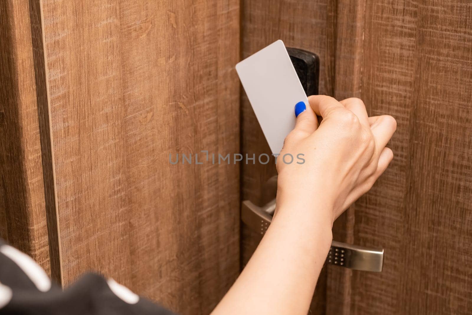 Woman hand puts key card to panel opening hotel room door. Female person with blue nails opening door