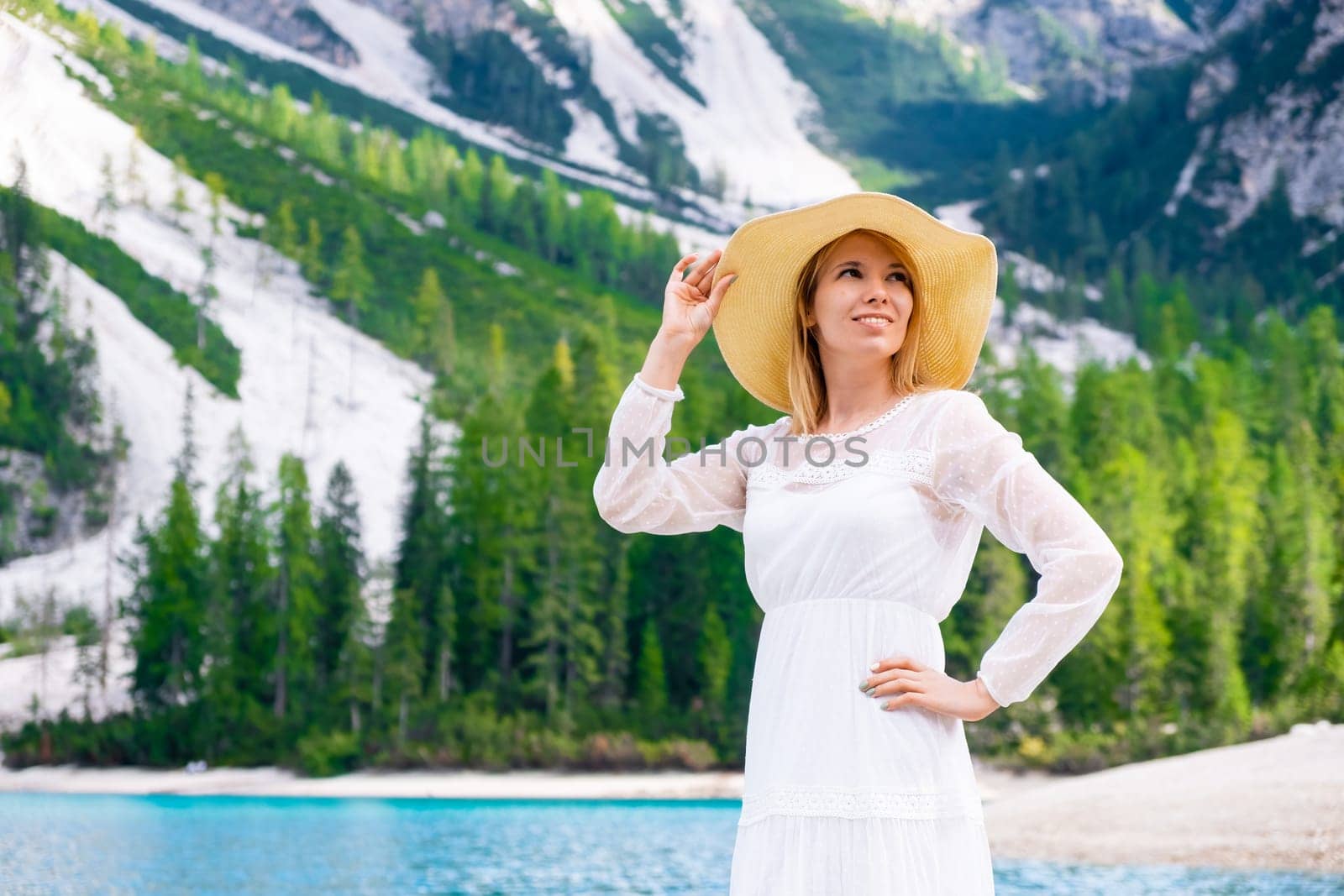 Smiling young woman on the Lake Braies in a white fluttering dress and hat on a sunny day