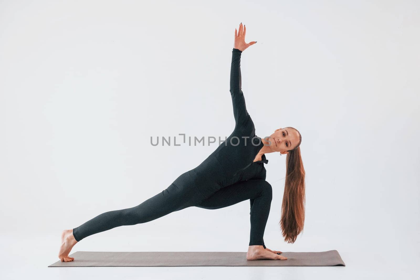Side view. Young woman in sportive clothes doing gymnastics indoors.