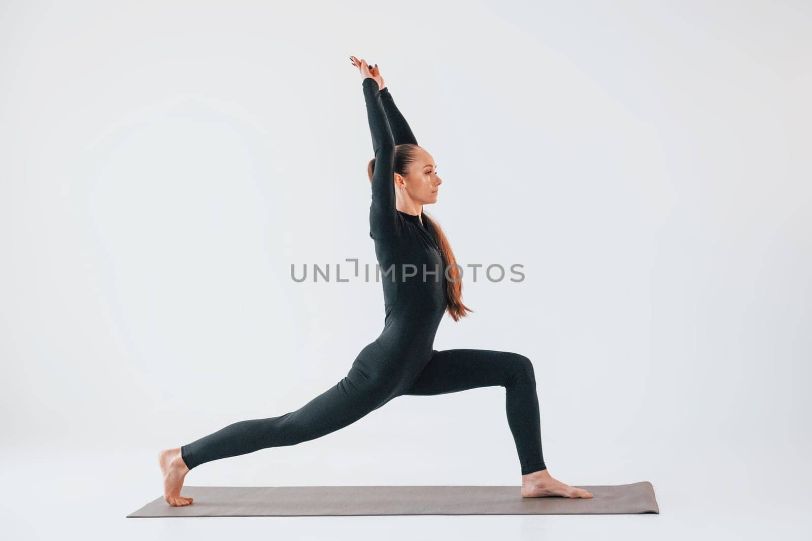 Side view. Young woman in sportive clothes doing gymnastics indoors.