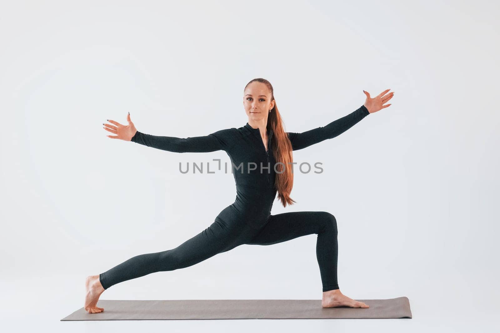 Side view. Young woman in sportive clothes doing gymnastics indoors.