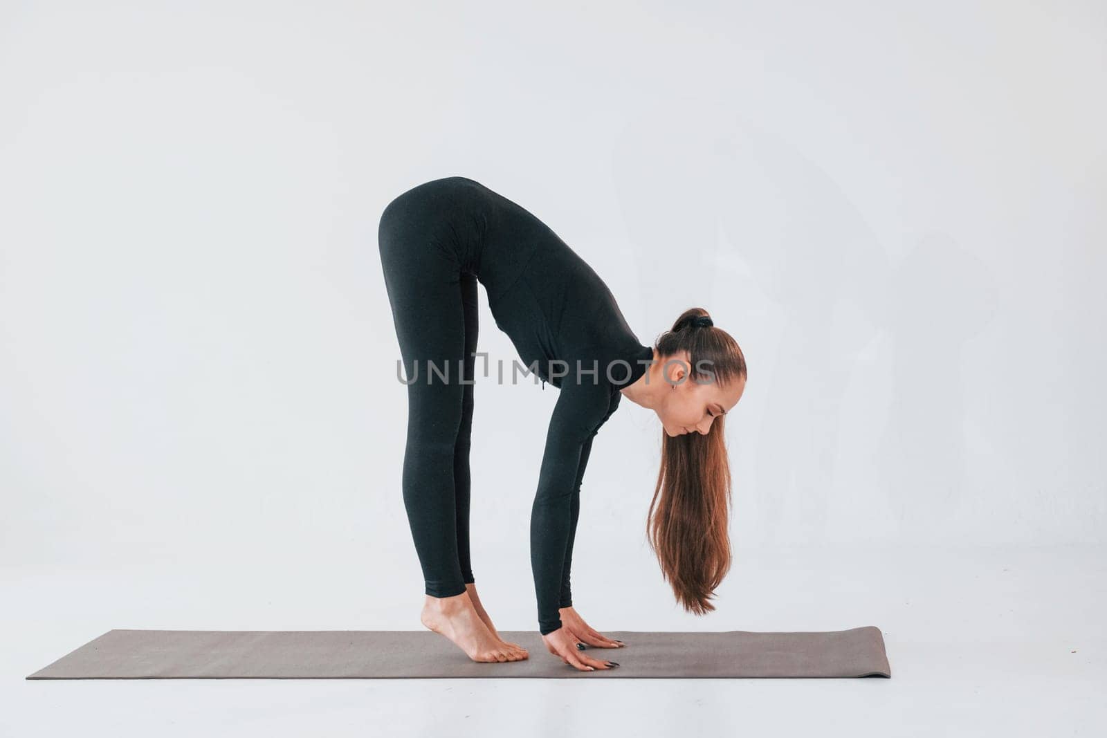 Side view. Young woman in sportive clothes doing gymnastics indoors.
