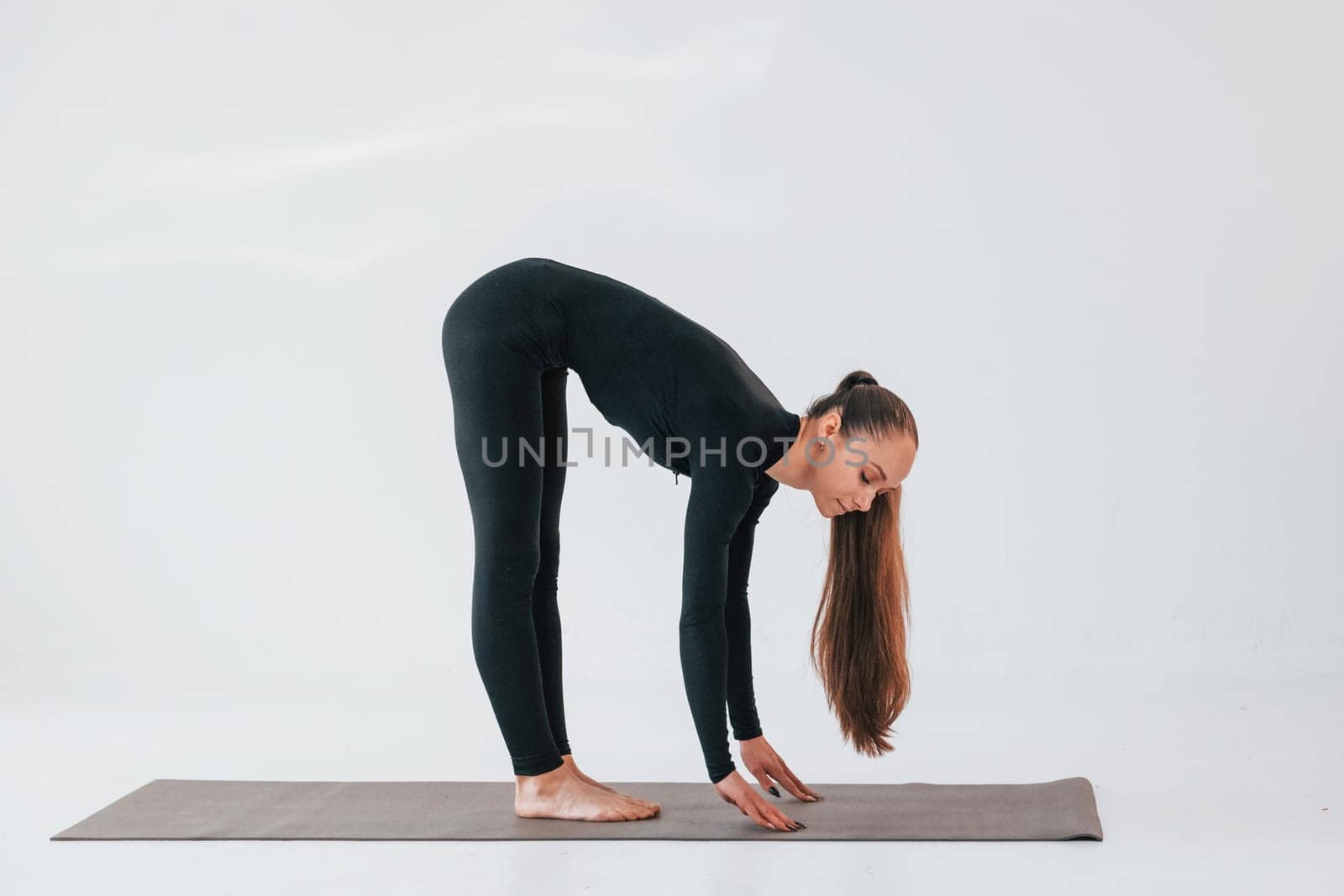 In black clothes. Young woman in sportive clothes doing gymnastics indoors.
