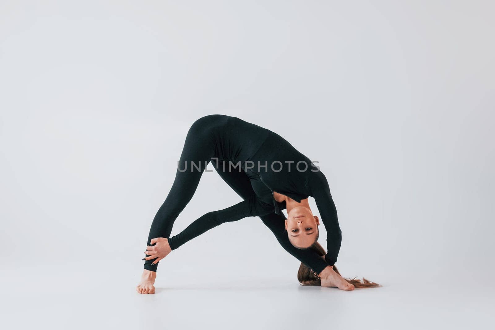 In black clothes. Young woman in sportive clothes doing gymnastics indoors.
