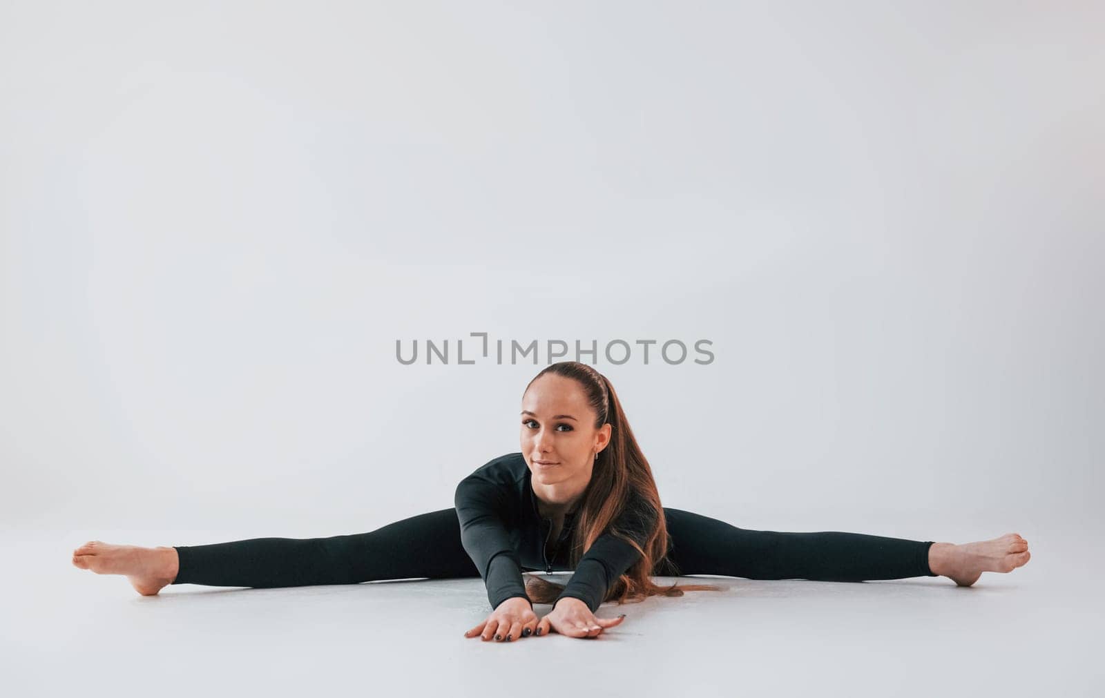 In black clothes. Young woman in sportive clothes doing gymnastics indoors.