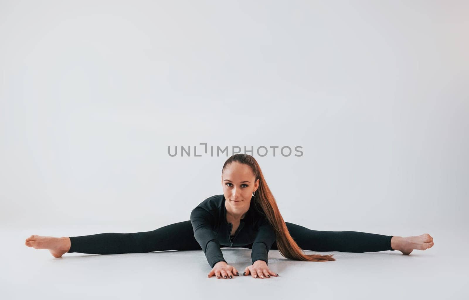 In black clothes. Young woman in sportive clothes doing gymnastics indoors.