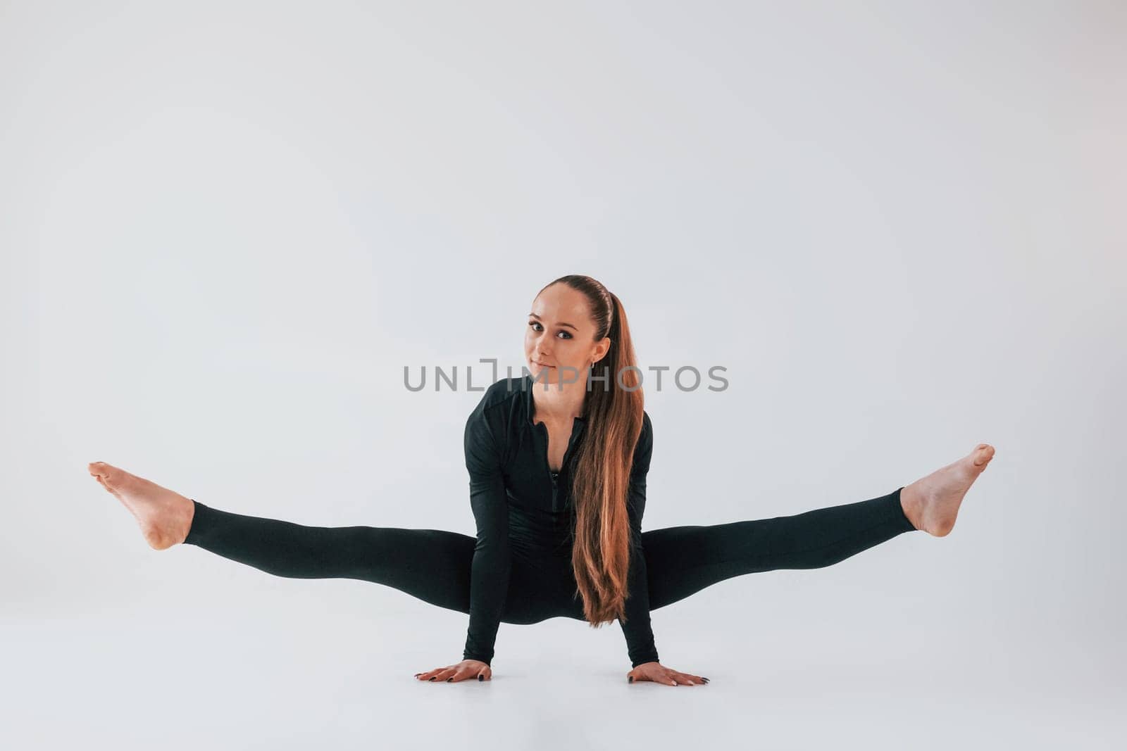 In black clothes. Young woman in sportive clothes doing gymnastics indoors.