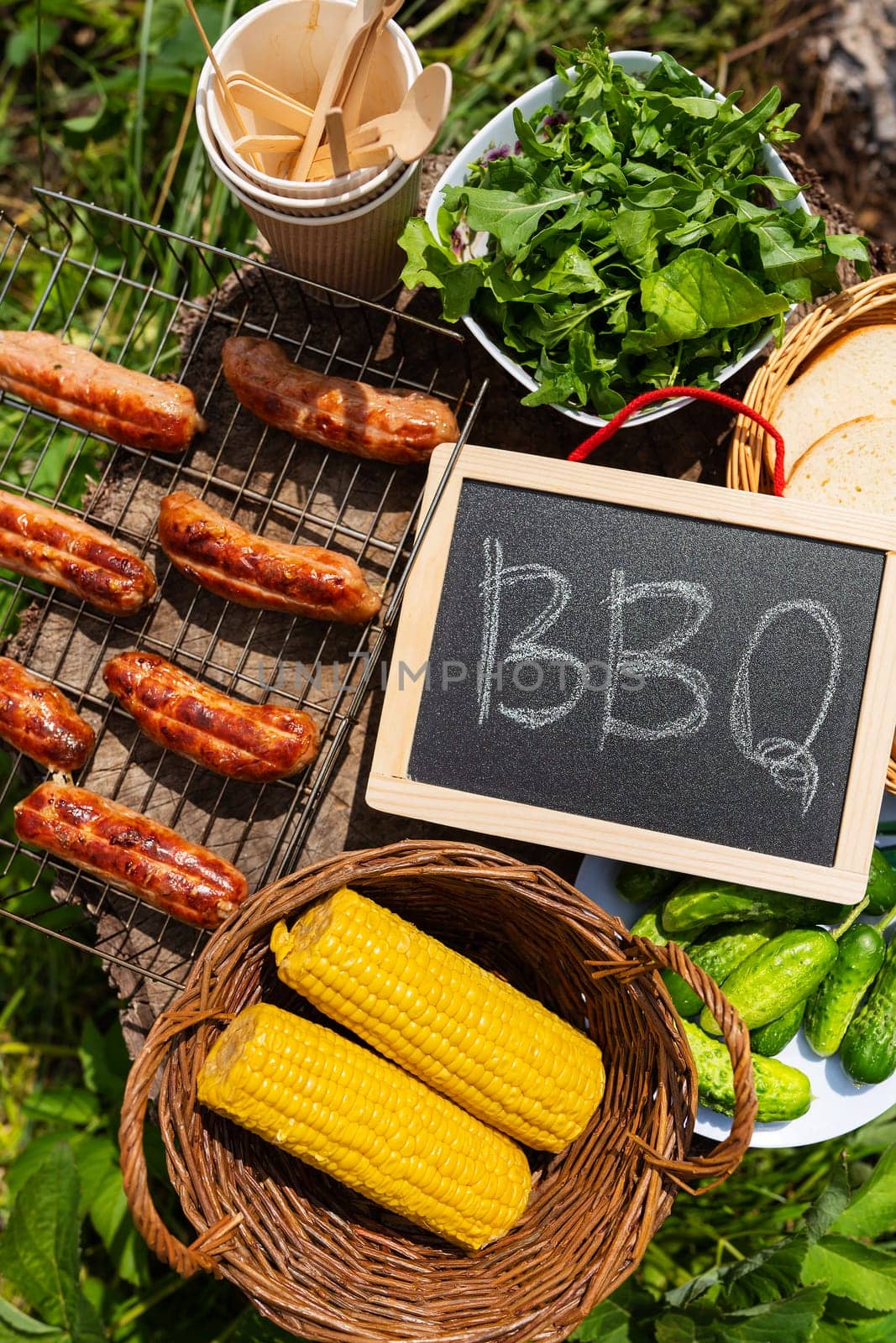 Close-up of fried sausages, corn, salad, vegetables with barbecue sign. Rest in nature, picnic, weekend