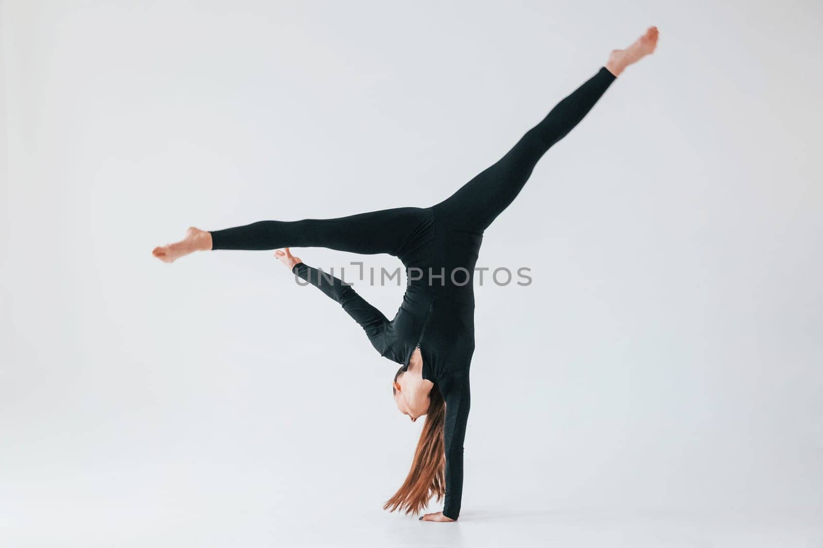 Professional exercises. Young woman in sportive clothes doing gymnastics indoors.