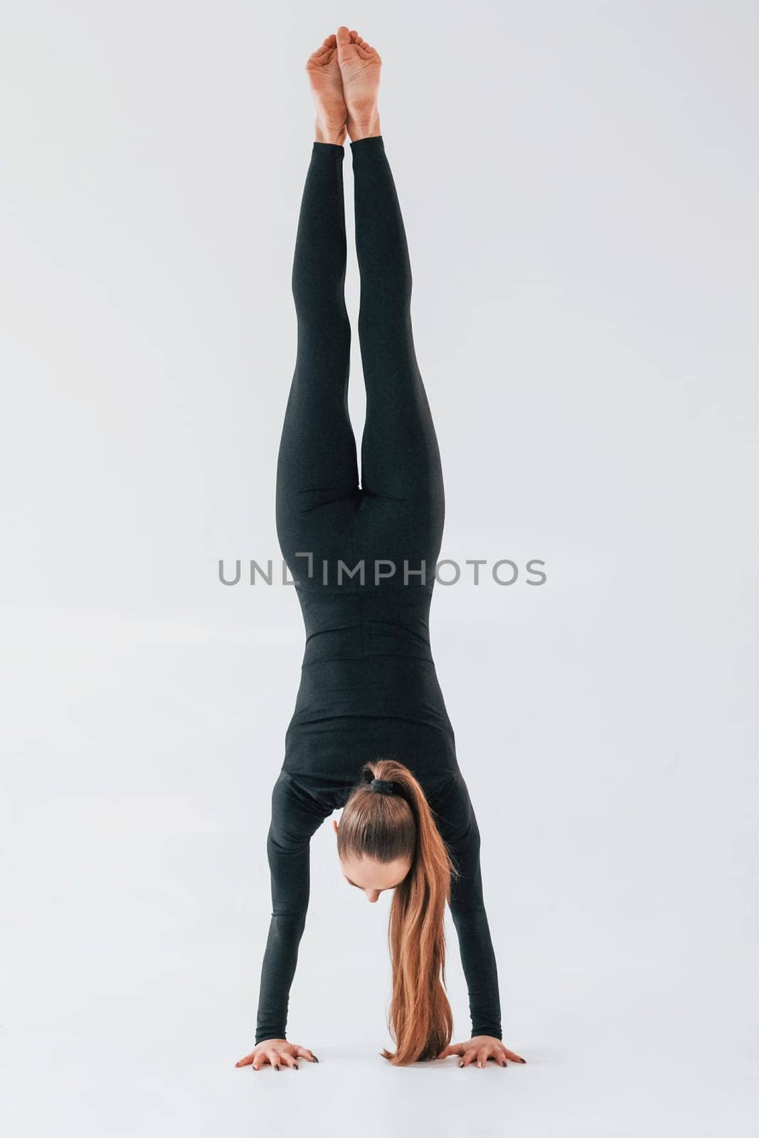 Professional exercises. Young woman in sportive clothes doing gymnastics indoors.