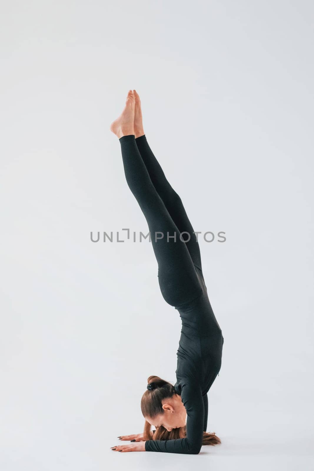 Practice routine. Young woman in sportive clothes doing gymnastics indoors.