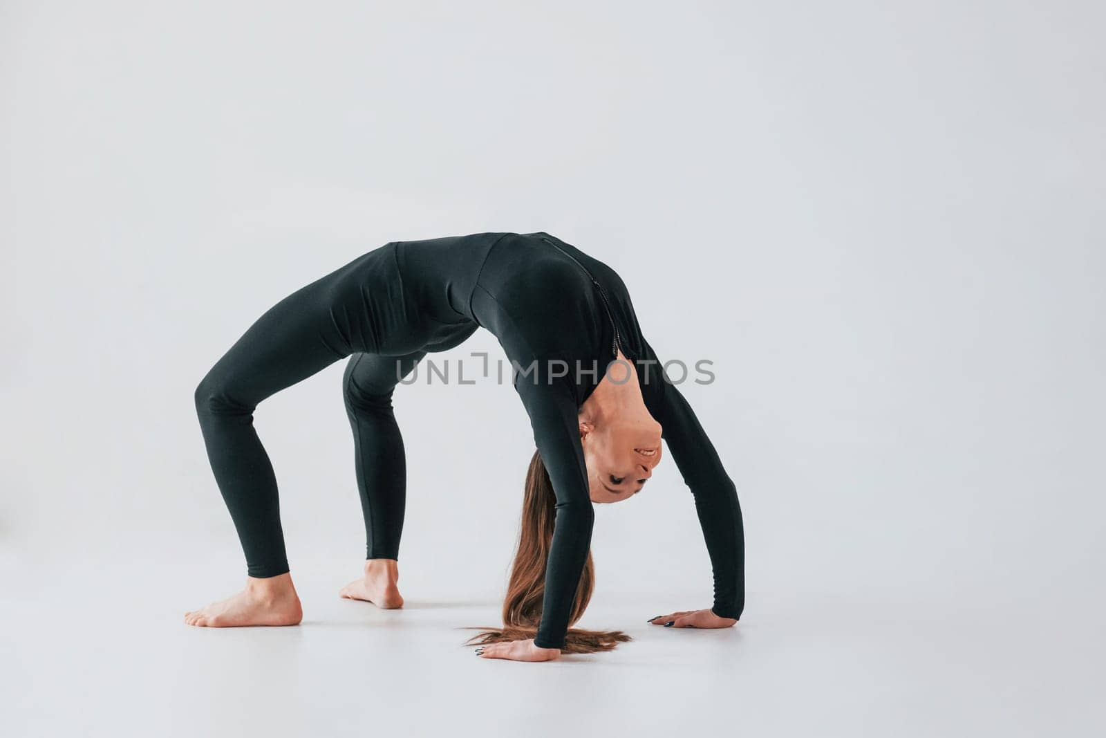 Against white background. Young woman in sportive clothes doing gymnastics indoors.