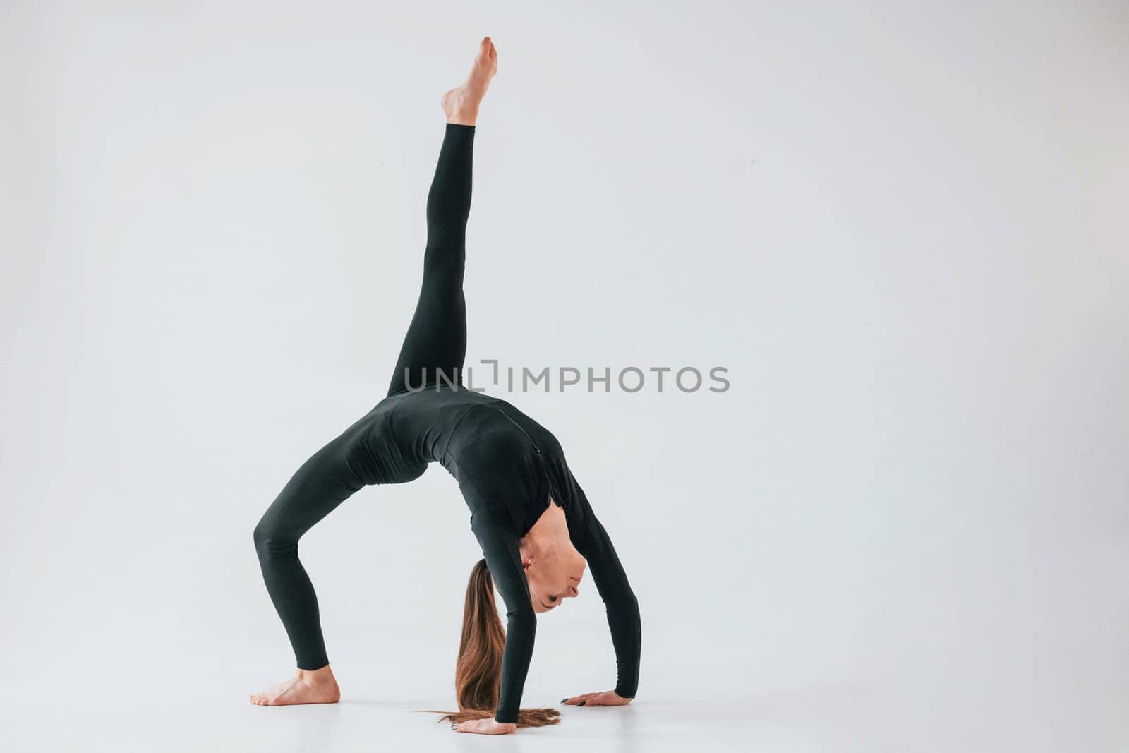 Against white background. Young woman in sportive clothes doing gymnastics indoors.