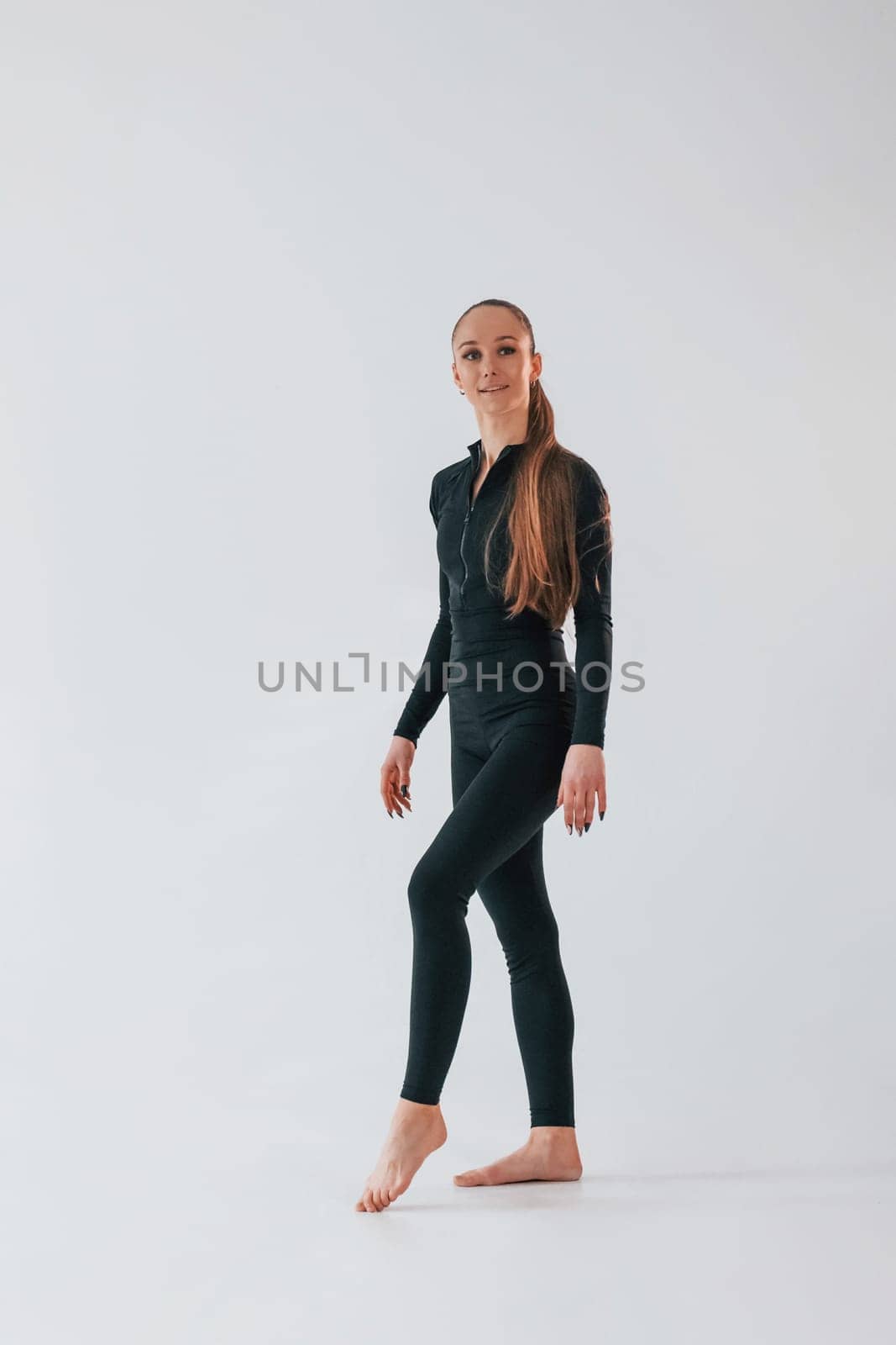 Against white background. Young woman in sportive clothes doing gymnastics indoors.