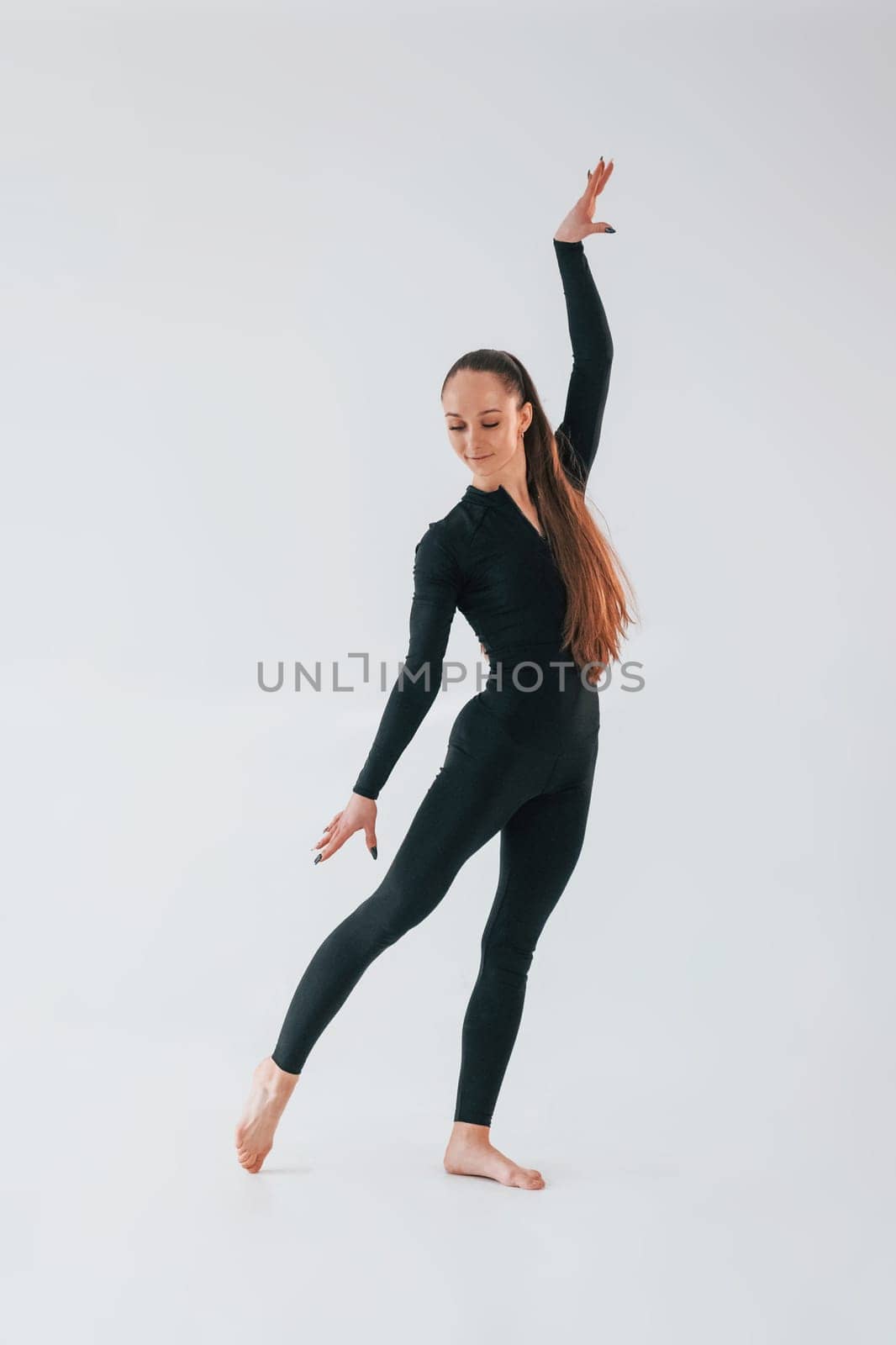 White background. Young woman in sportive clothes doing gymnastics indoors.
