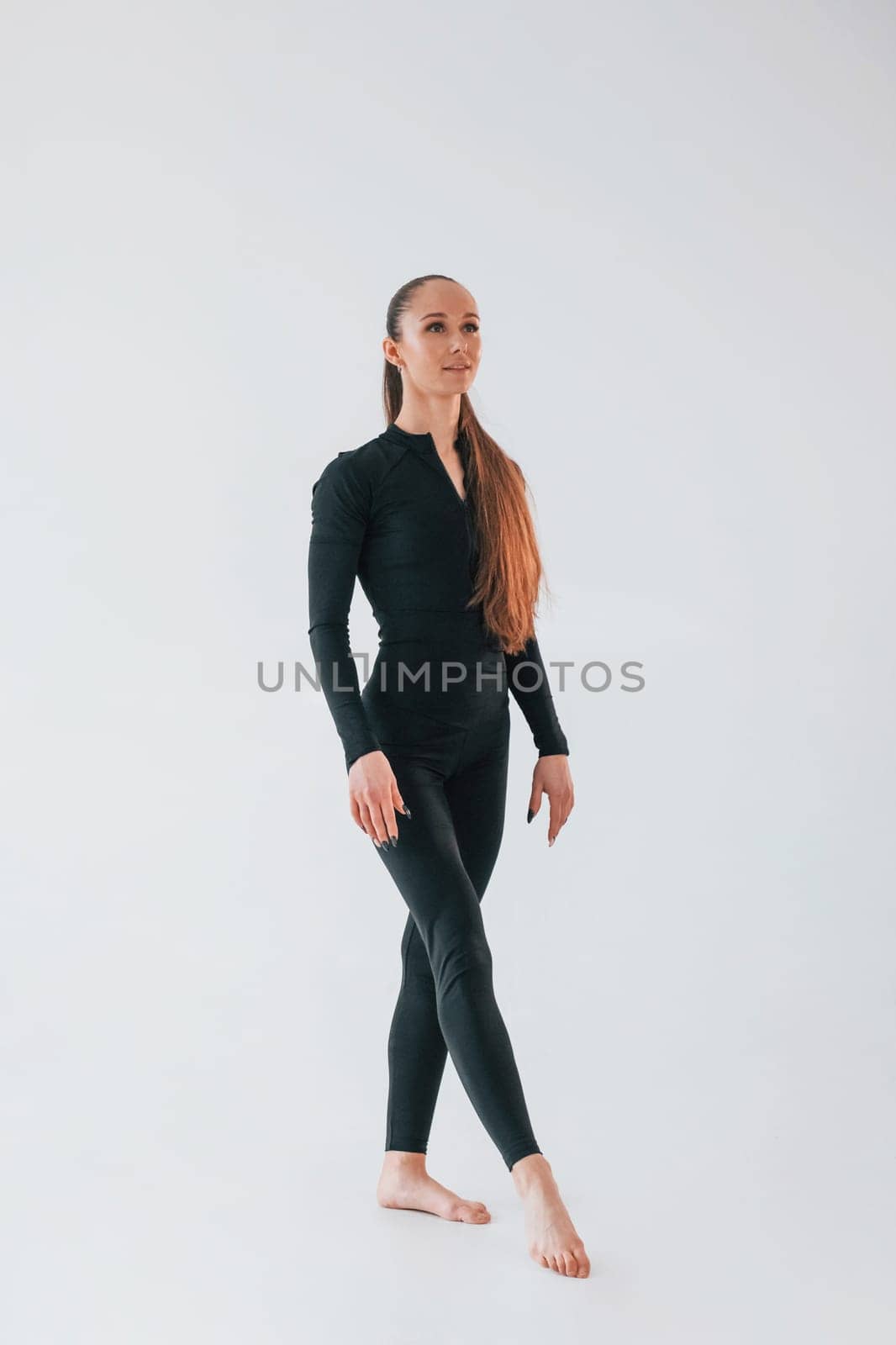 White background. Young woman in sportive clothes doing gymnastics indoors.