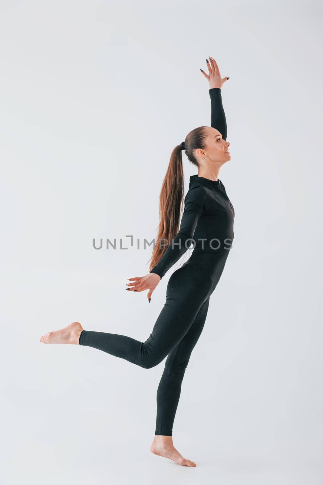 White background. Young woman in sportive clothes doing gymnastics indoors.