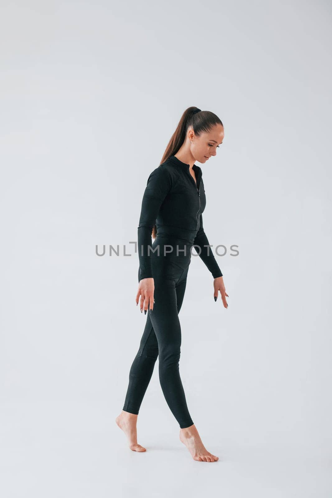 Standing in the studio. Young woman in sportive clothes doing gymnastics indoors.