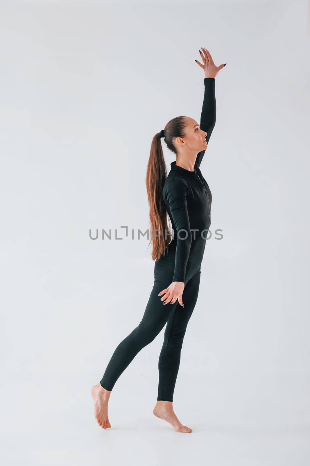 Standing in the studio. Young woman in sportive clothes doing gymnastics indoors.