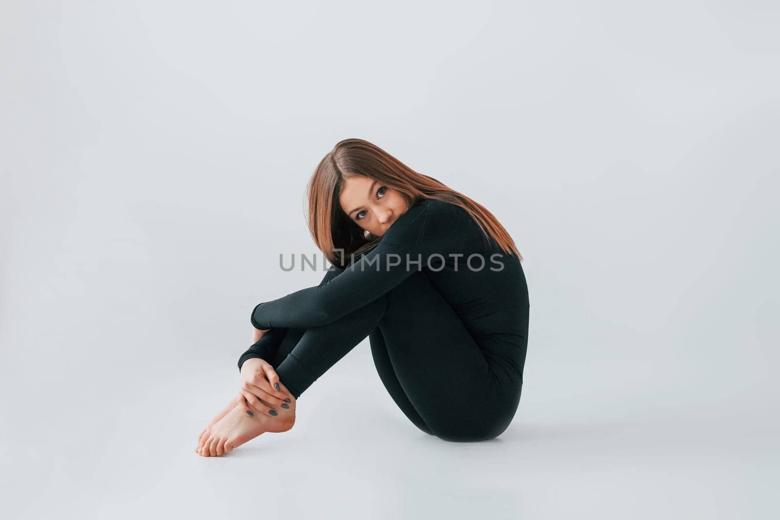 On the floor. Young woman in sportive clothes doing gymnastics indoors.