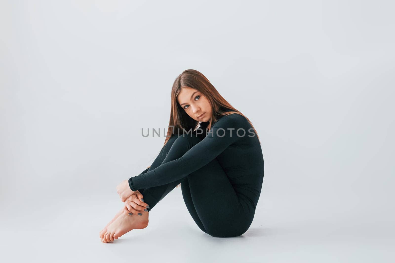 On the floor. Young woman in sportive clothes doing gymnastics indoors.