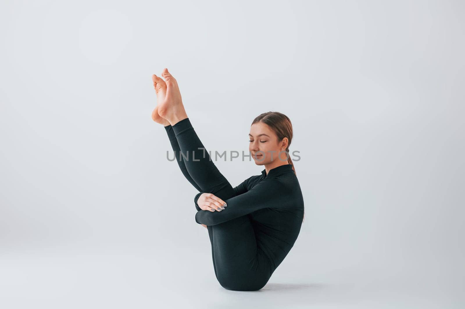 View from the side. Young woman in sportive clothes doing gymnastics indoors.