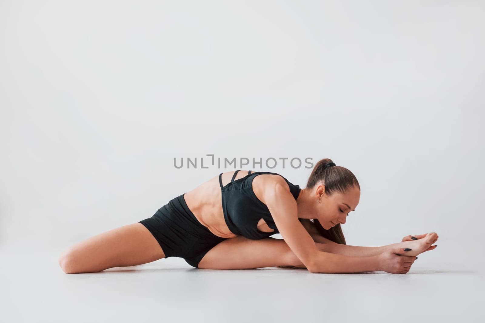 Stretching to the side. Young woman in sportive clothes doing gymnastics indoors.