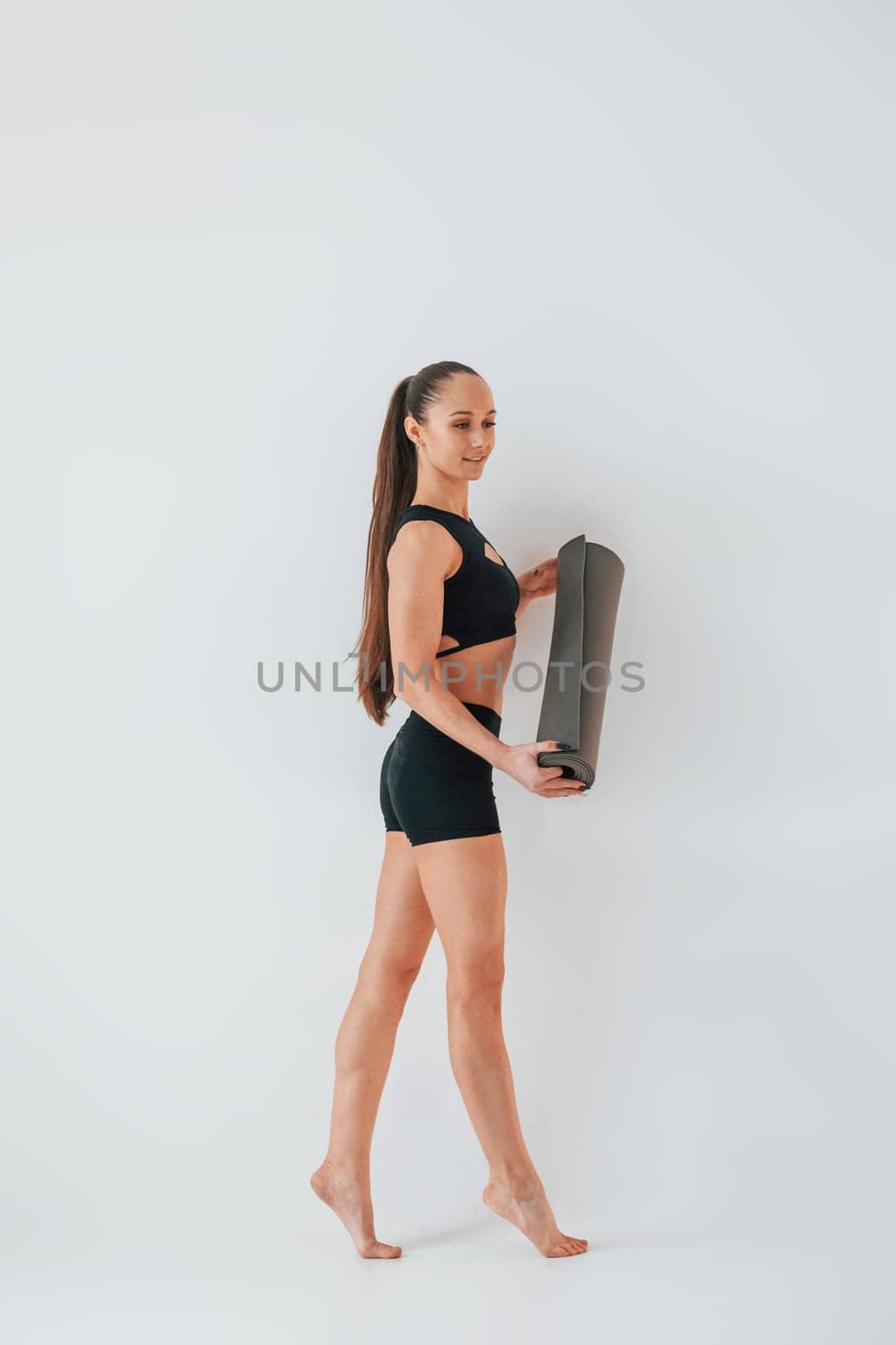 Standing and holding mat. Young woman in sportive clothes doing gymnastics indoors.