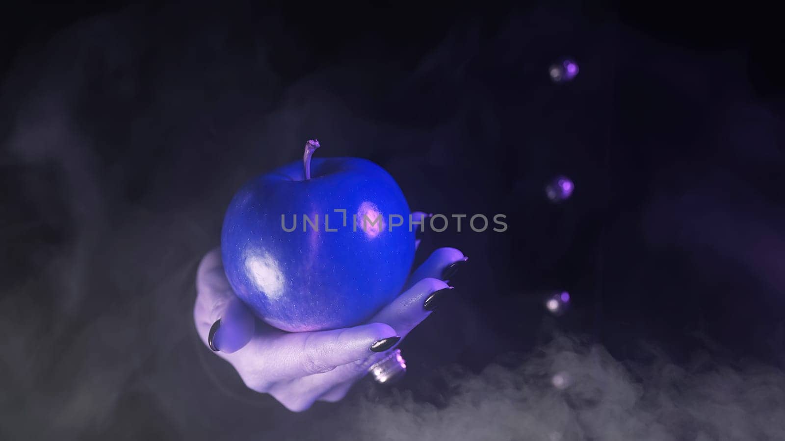 Woman as witch offers blue apple as symbol of toxic temptation, poison, sin. Fairy tale, white snow wizard concept. Spooky halloween, cosplay. Smoke, haze background. High quality photo