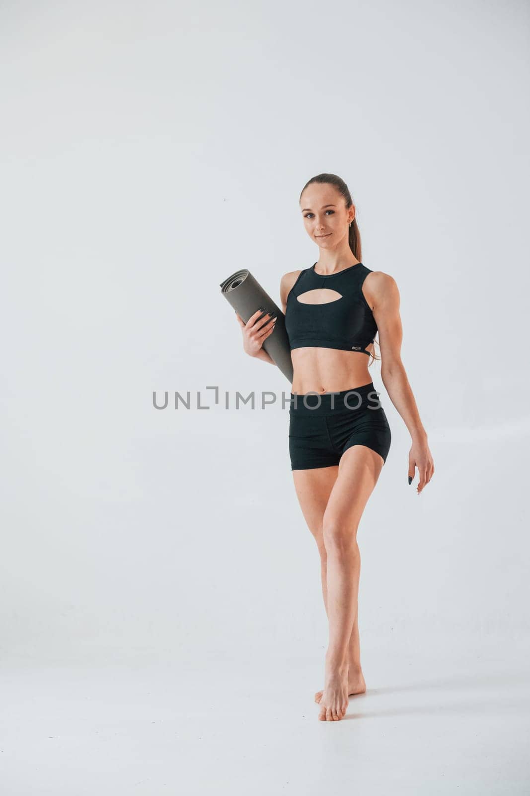 Holding yoga mat and standing. Young woman in sportive clothes doing gymnastics indoors.