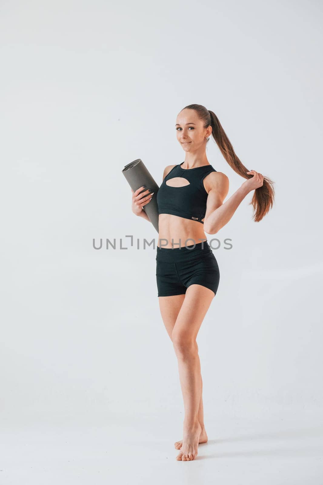 Holding yoga mat and standing. Young woman in sportive clothes doing gymnastics indoors.