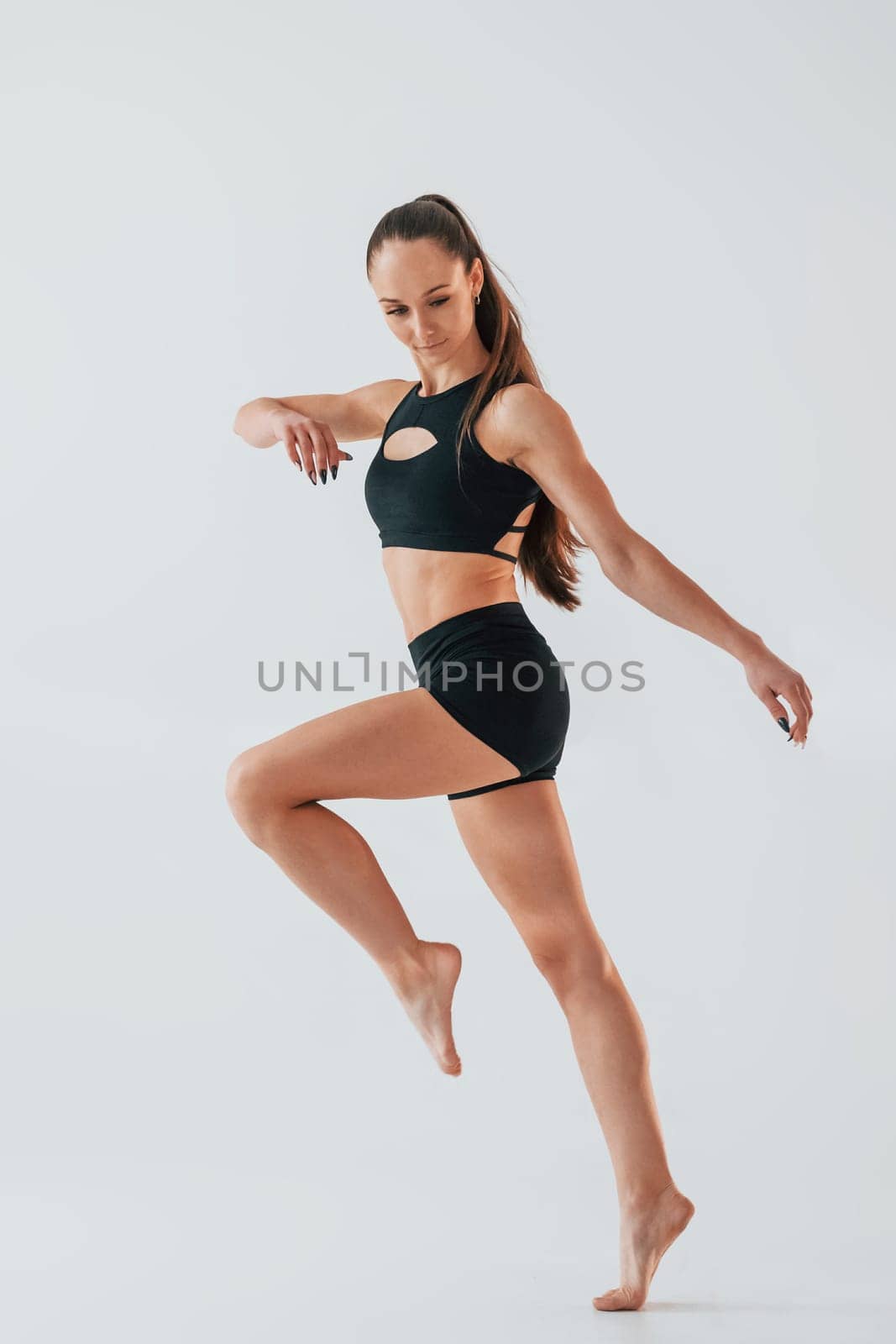 In the studio against white background. Young woman in sportive clothes doing gymnastics indoors.