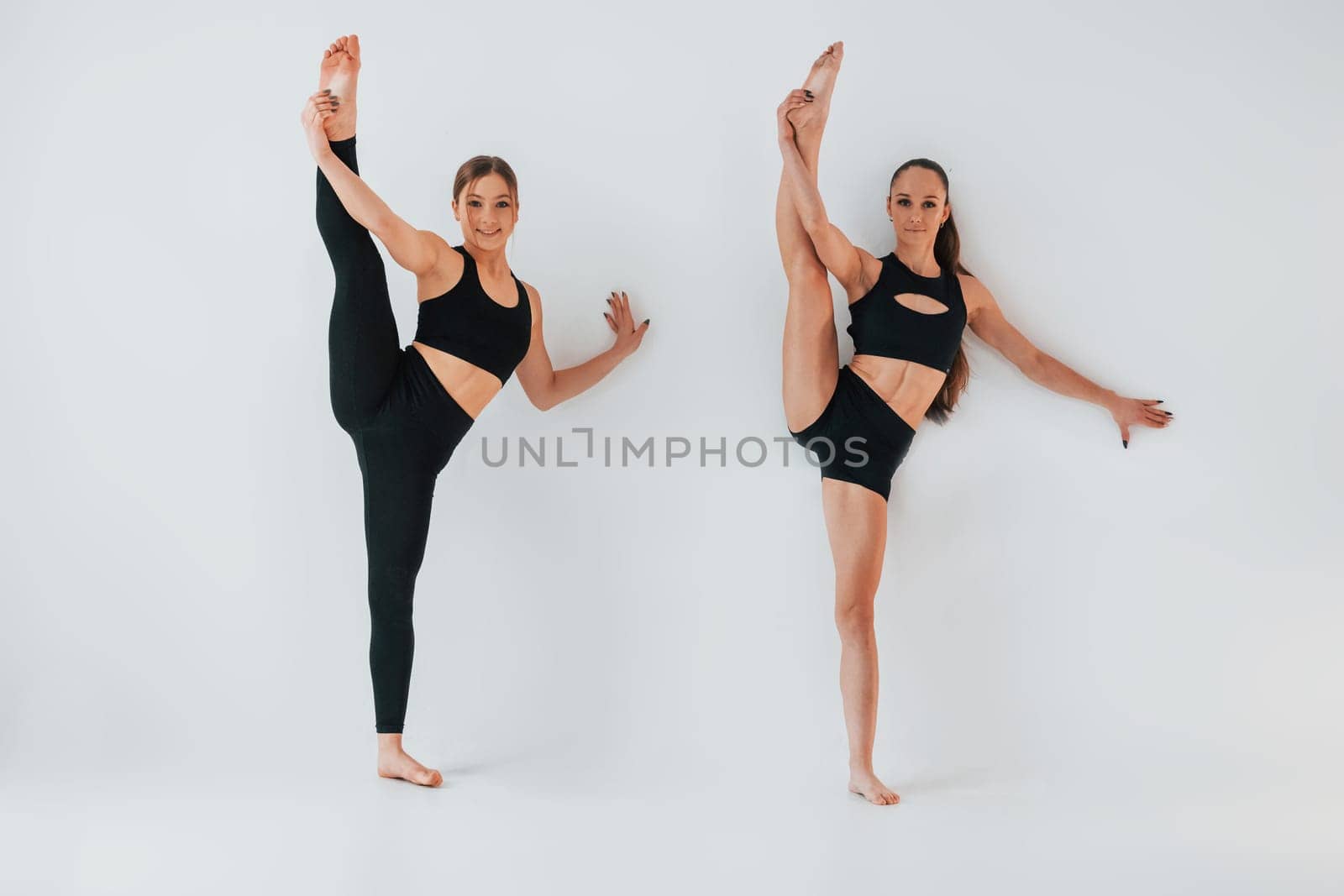 Two young women in sportive clothes is together indoors against white background.