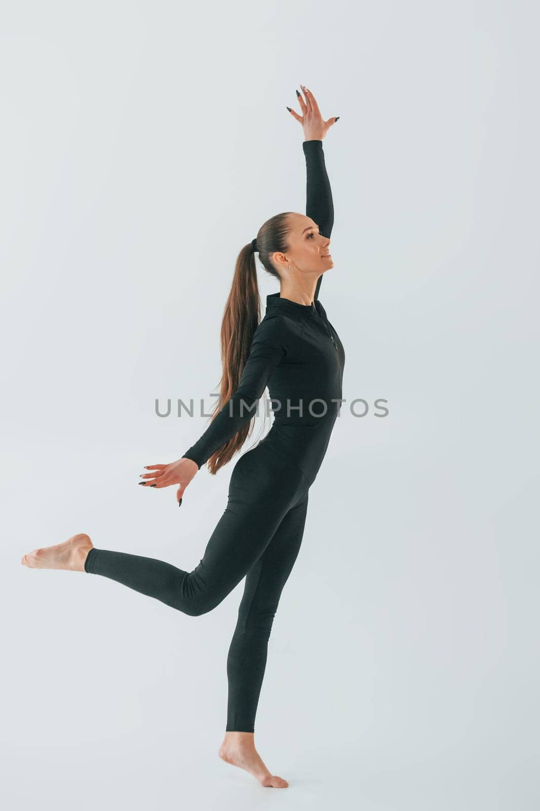 In black sportive clothes. Young woman doing gymnastics indoors.
