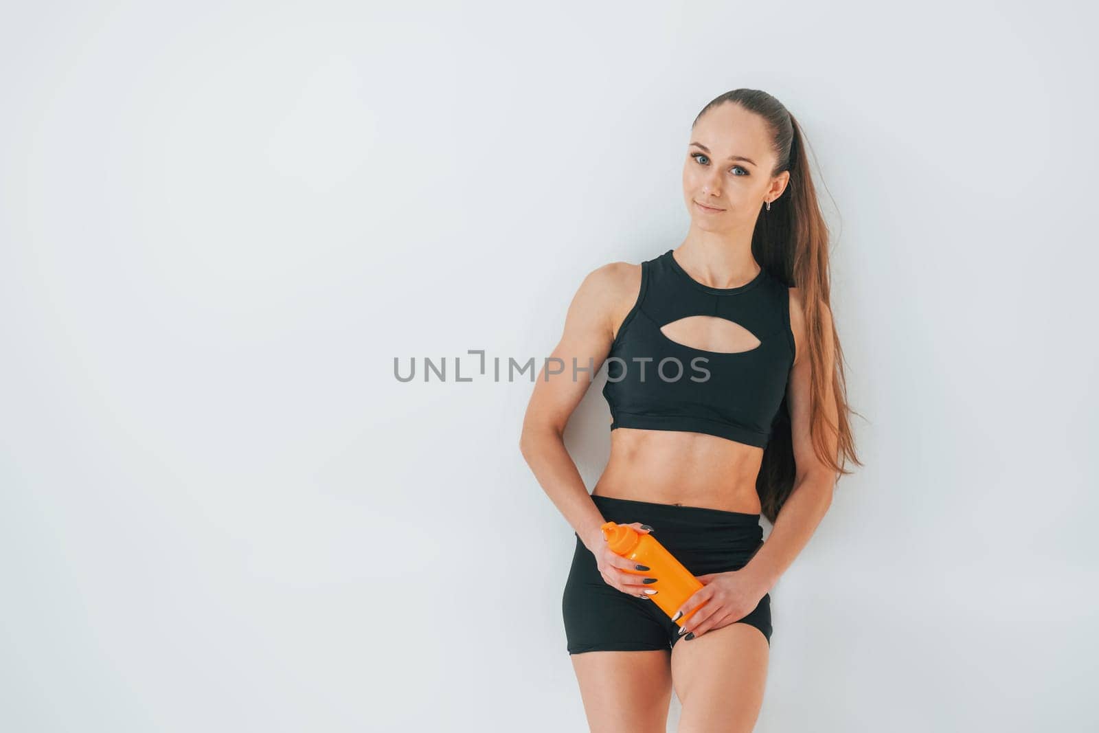 Standing against white background. Young woman in sportive clothes doing gymnastics indoors.