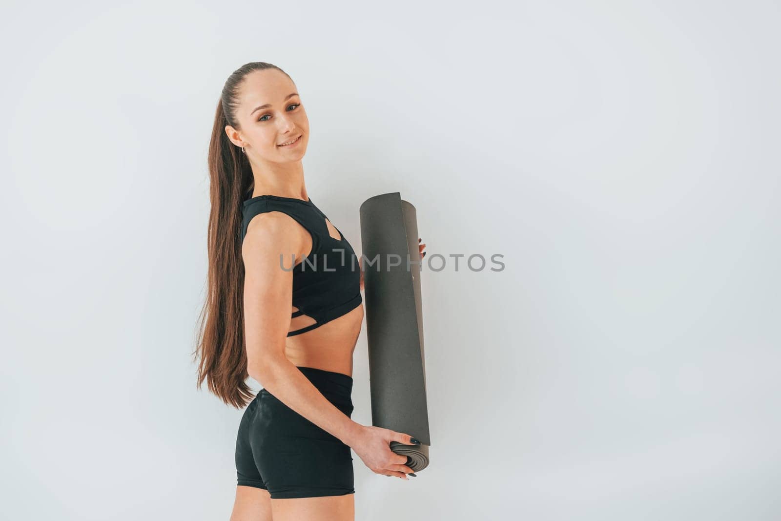 Standing against white background. Young woman in sportive clothes doing gymnastics indoors.
