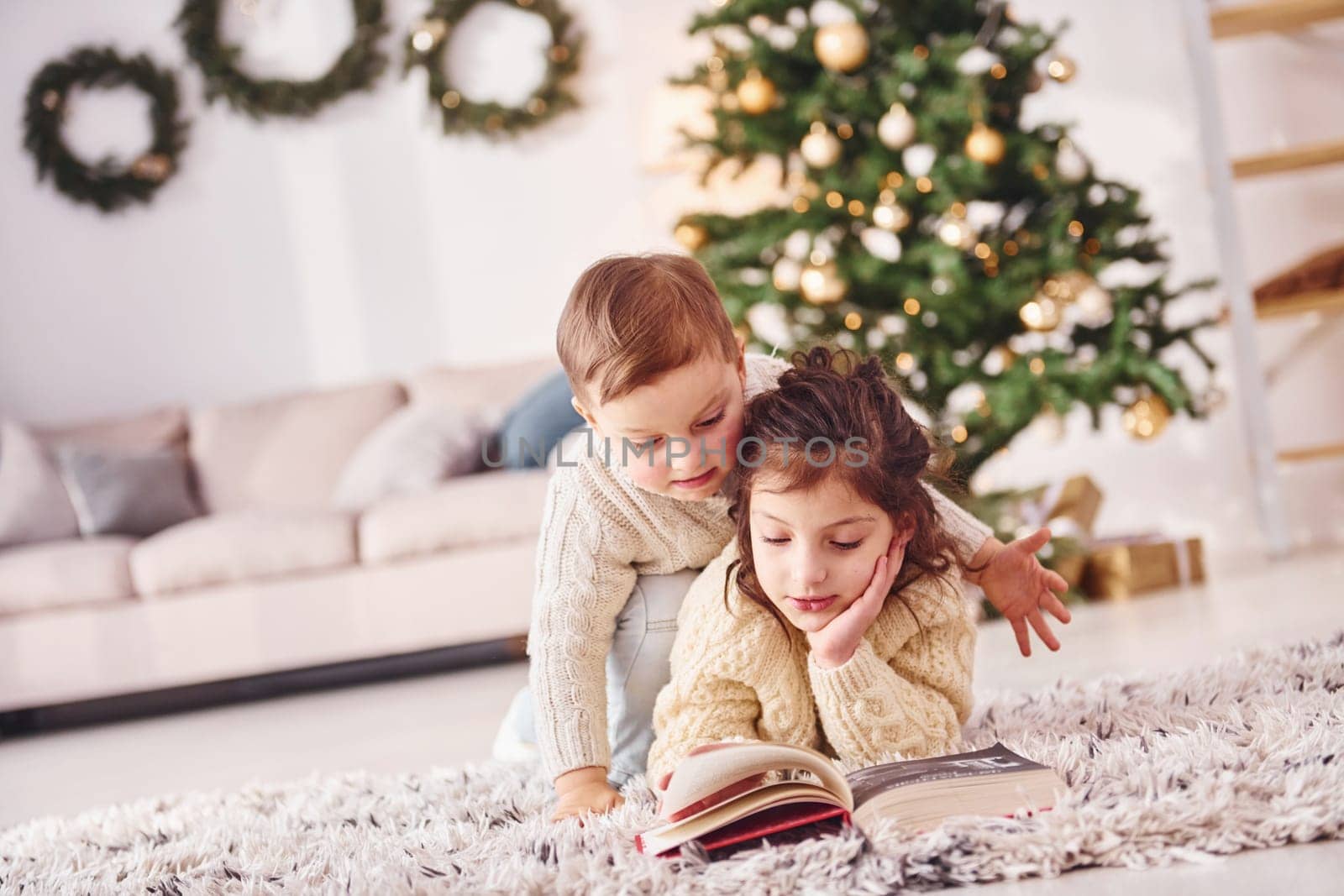 Laying down on the ground. Little brother and sister is at christmas decorated room together.