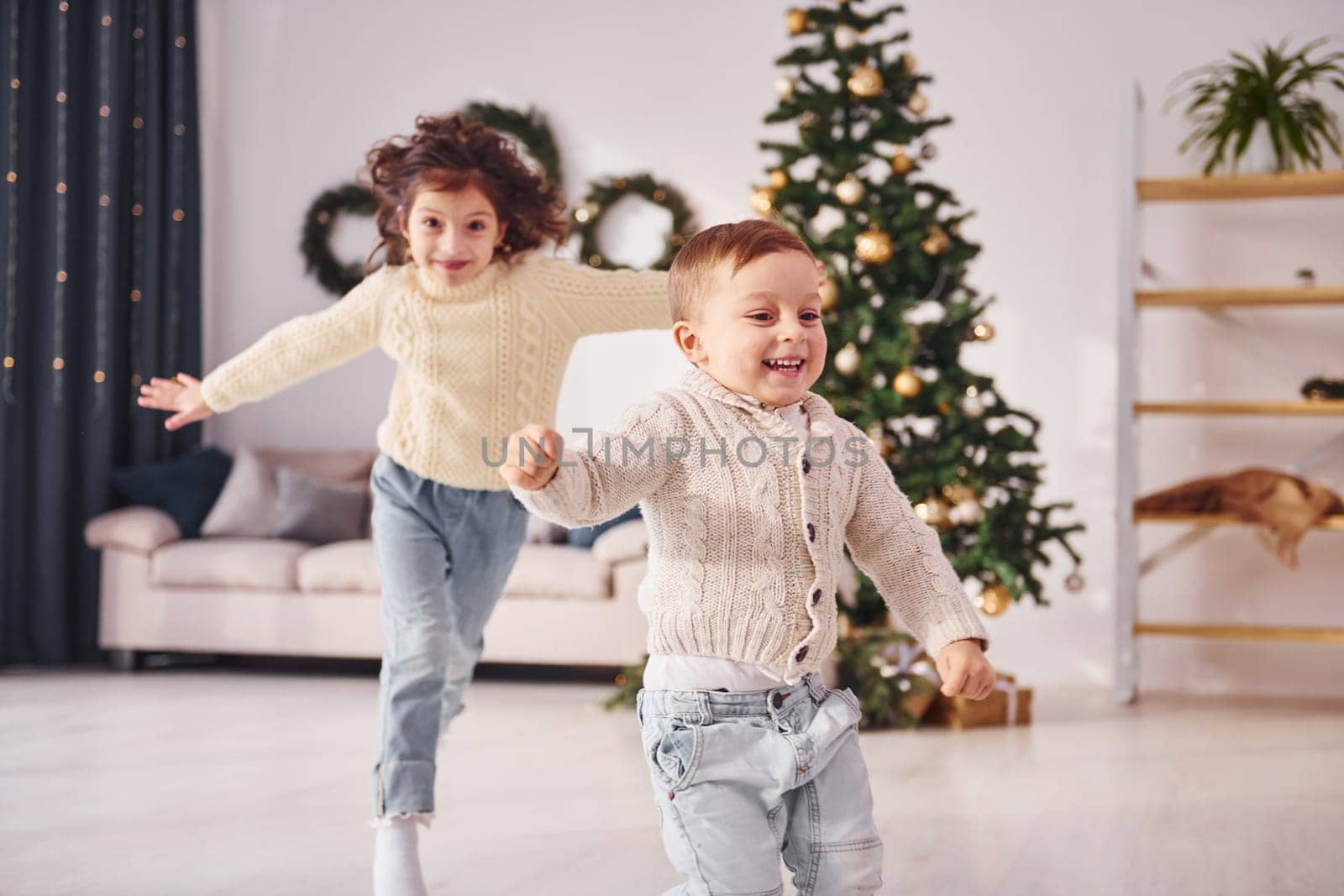 Active time spending. Little brother and sister is at christmas decorated room together.