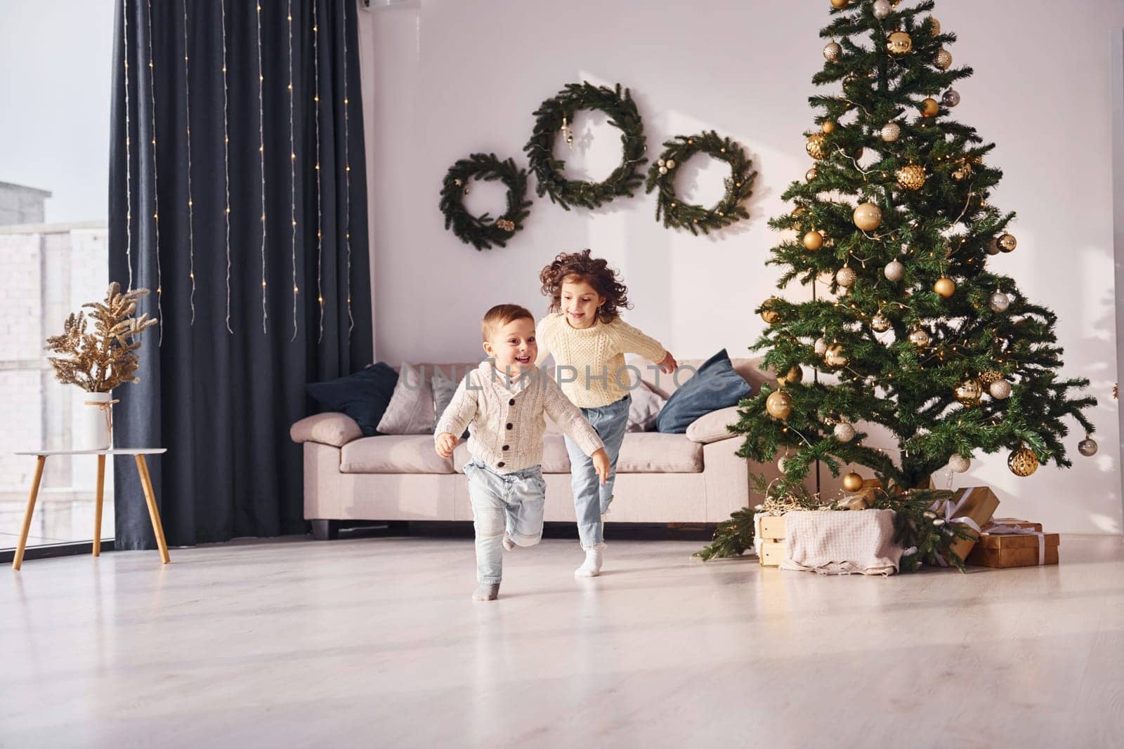 Active time spending. Little brother and sister is at christmas decorated room together.