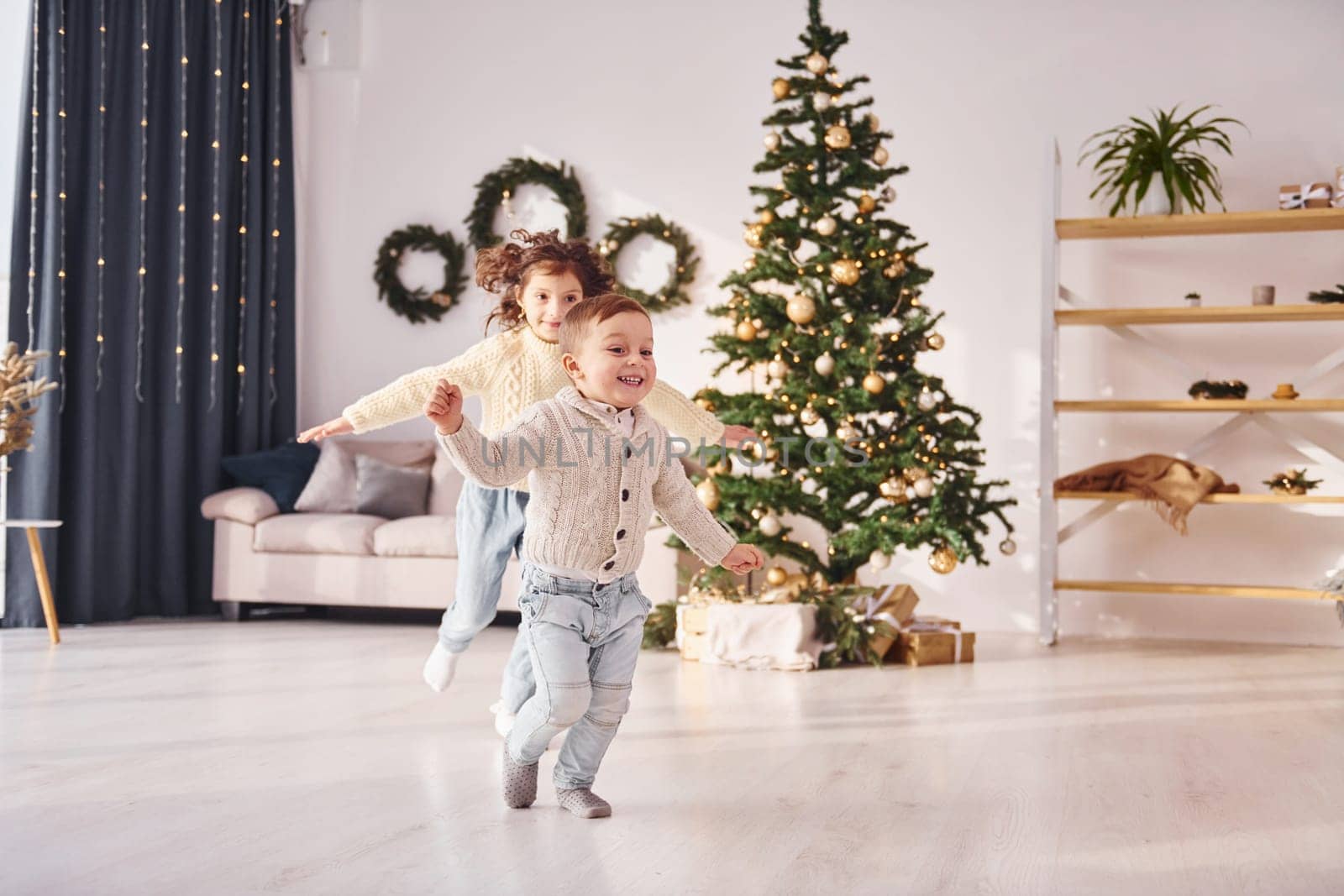 Running together. Little brother and sister is at christmas decorated room.