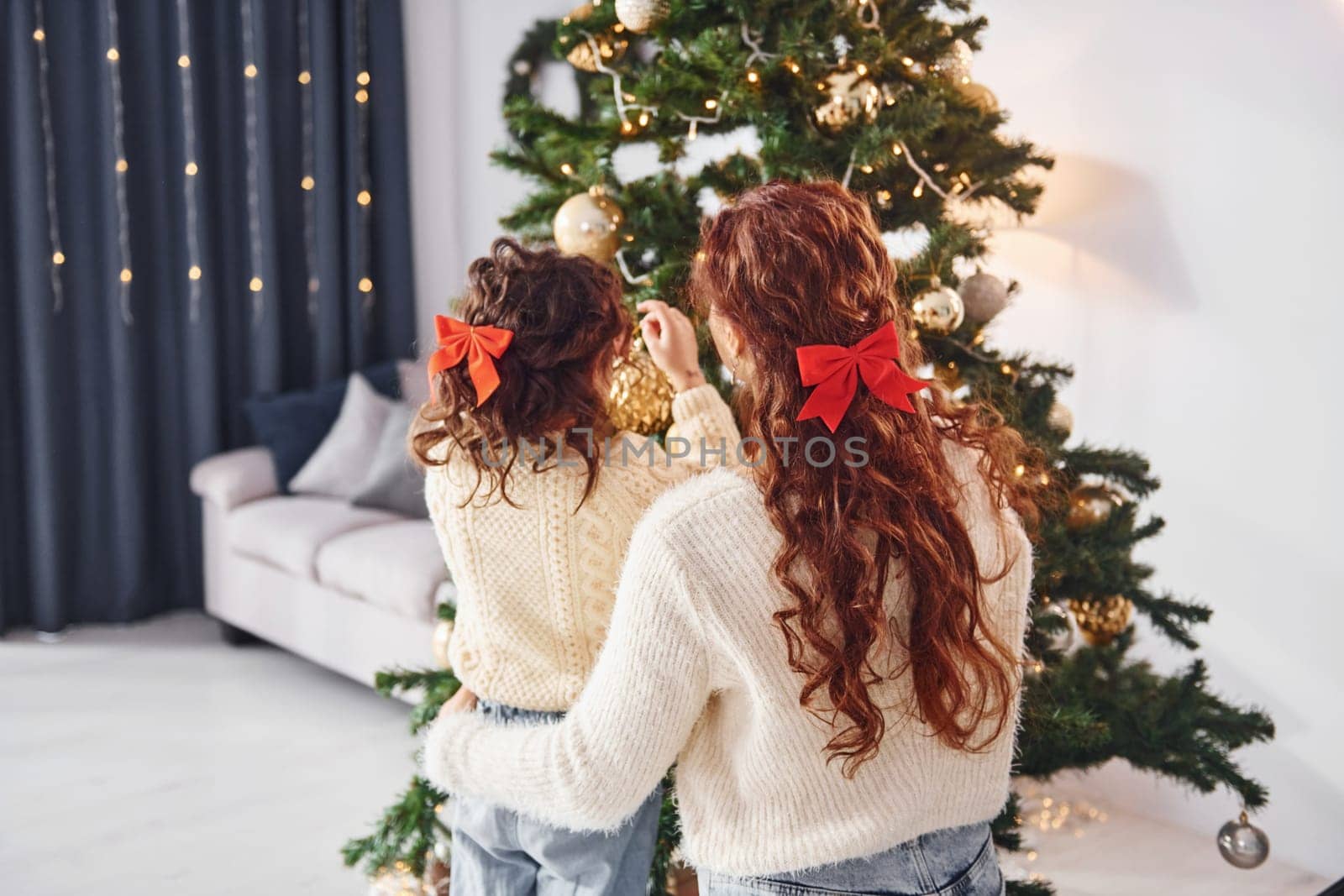 Rear view. Mother with her little daughter is at home. Christmas decorations.